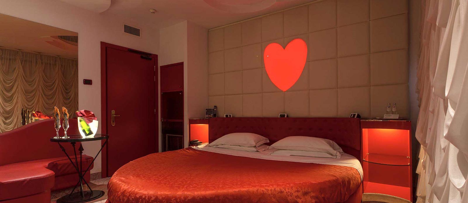 Motel K Junior Suite Cupido , letto rotondo, bottiglia di champagne in secchiello del ghiaccio appoggiato sula tavolo assieme a 2 bicchiere camera a tema Amore